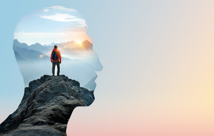 Head silhouette containing a mountain scene with a person standing on a rocky summit